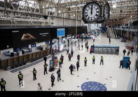 (210324) -- LONDON, March 24, 2021 (Xinhua) -- Travellers, police officers and rail staff observe one minute's silence at Waterloo Station in London, Britain, on March 23, 2021. Britain on Tuesday marked one year since British Prime Minister Boris Johnson announced the first coronavirus lockdown in the country last year. On March 23, 2020, Johnson unveiled measures to stop the spread of COVID-19. A national minute's silence was held at midday as part of a day of reflection. Britons are also encouraged to stand on their doorsteps at 2000 GMT with phones, candles and torches to remember the p Stock Photo