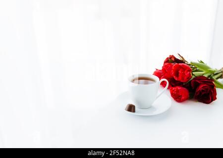 Red tulips bouquete on table, white coffee cup. Concept for greeting card for mothers day, international womans day or valentines day concept, birthda Stock Photo