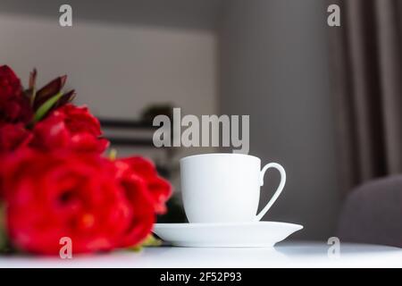 Red tulips bouquete on table, white coffee cup. Concept for greeting card for mothers day, international womans day or valentines day concept, birthda Stock Photo