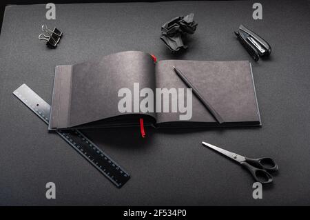 Black office on a black table. Black notebook and stationery. Black office supplies. Top view at an angle. Stock Photo