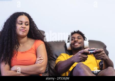 Boy is playing playstation computer game and woman girlfriend is angry for him. Technology and relationship concept. Focus on joystick Stock Photo