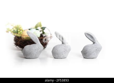 Three small stone rabbits with defocused bird nest and greenery. Tiny adorable simple Easter bunnies. Animal or Easter themed table decoration. Isolat Stock Photo