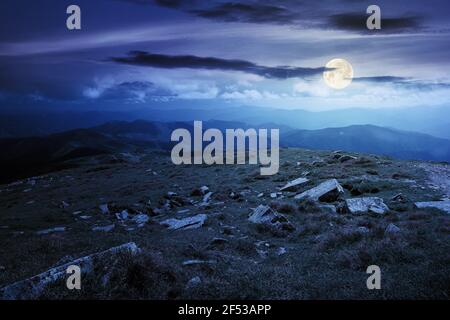 carpathian summer mountain landscape at night. beautiful countryside with rocks on the grassy hill in full moon light clouds on the blue sky. wonderfu Stock Photo
