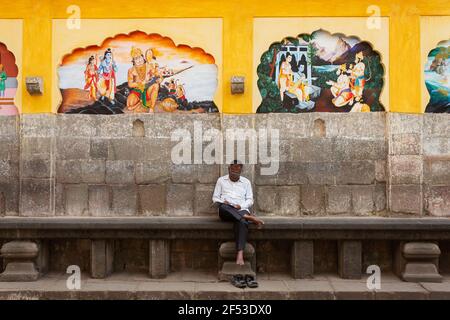 Man on wooden bench solving puzzle in Newspaper at  Tulsibaugh, Pune, Maharashtra, India. Stock Photo