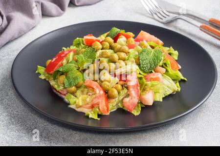 Salad of green tomato leaves and canned peas seasoned with sauce on a black plate. Spring fresh diet salad Stock Photo