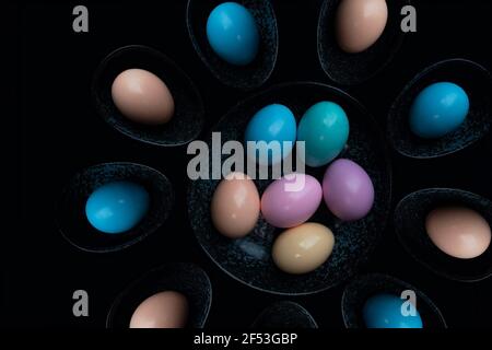 Top view pastel colored Easter eggs in a dark granite plate against Black background. Stock Photo