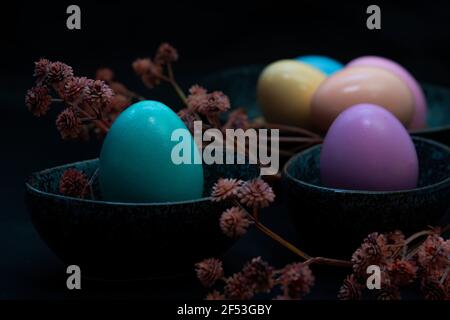 Side view of  flowers and pastel colored Easter eggs in a dark granite plate against Black background. Stock Photo