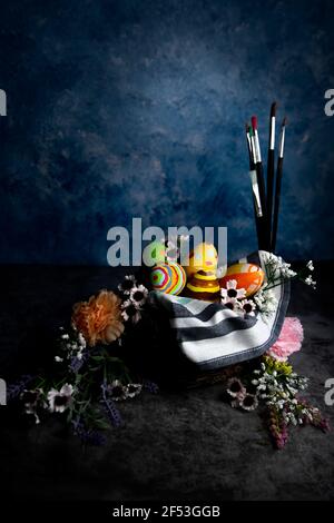 Paint brushes and colored Easter eggs in a straw corp with flowers ,Still life ,selective focus. Stock Photo