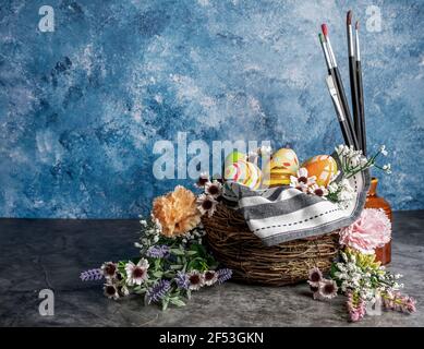 Paint brushes and colored Easter eggs in a straw corp with flowers ,Still life ,selective focus. Stock Photo