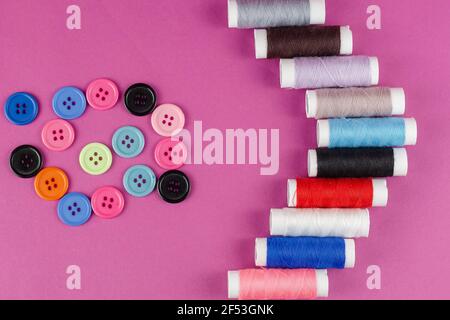 Multicolored thread spools and buttons on purple background. A set of thread. Ten spools. Random buttons. Top view, flatlay. Stock Photo