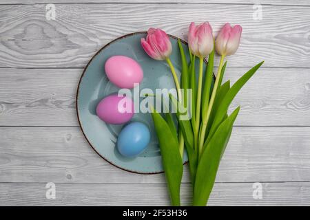Pastel colored Easter eggs in blue ,pink and three tulips on a blue plate and white colored wooden table. Stock Photo