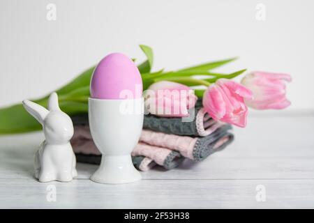 Front view of white Porcelain Egg Cups with pink Easter egg and porcelain Easter bunnies and  pastel colored pink white tulips.On a white background . Stock Photo