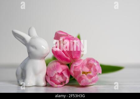 Front view of  porcelain Easter bunnies, pastel colored pink white tulips. On a white background . Stock Photo