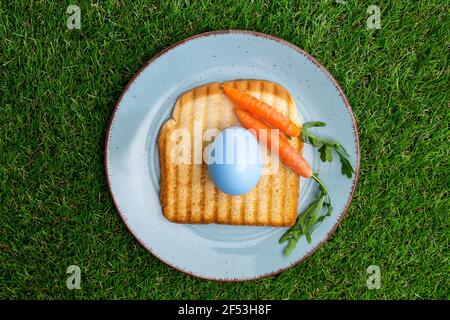 Top view of colored Easter egg over a toasted bread in plate with baby Carrot. Stock Photo