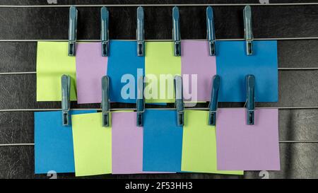The paper sticky notes hanging from clothespins. Set of multicolored blank square stickers on black background. No people. Stock Photo