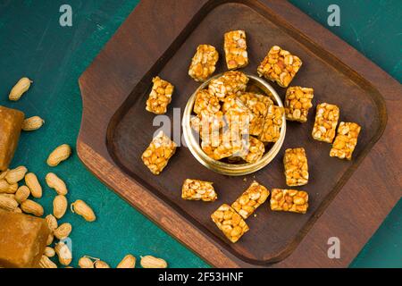 Peanut bar,crunchy sweet peanut bar which is very healthy  snack,arranged in a wooden base with some peanut and jaggery on the dark green texture back Stock Photo