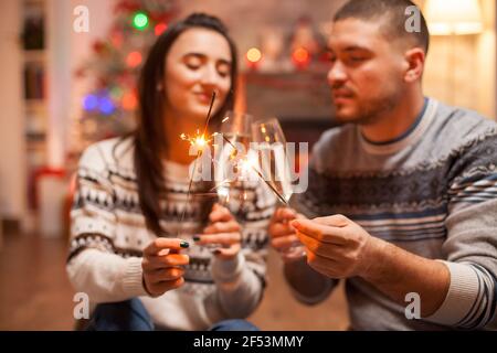 Happy couple clinking glasses of champagne and holding hand fireworks on christmas. Stock Photo