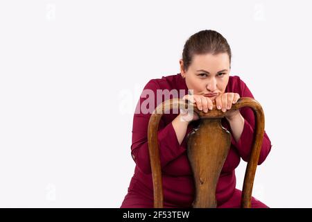 Portrait of a tired large size businesswoman sitting in an antique wooden chair. Gray background and side space. Stock Photo