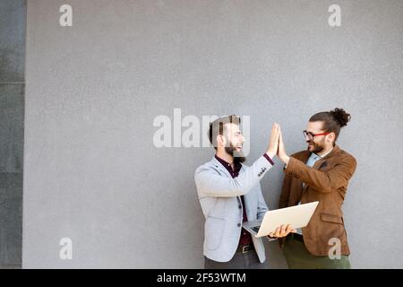 Positive successful business specialists discussing plan with laptop outdoors. Stock Photo