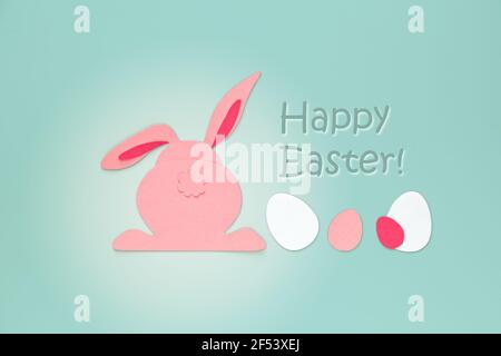 Easter creativity. Cut out paper rabbit and eggs on a blue background, back view. The inscription "Happy Easter". Easter concept. Stock Photo