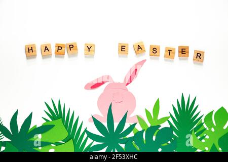 Easter creativity. Cut out paper rabbit, back view. Carved tropical leaves. The inscription "Happy Easter". Easter concept. Stock Photo