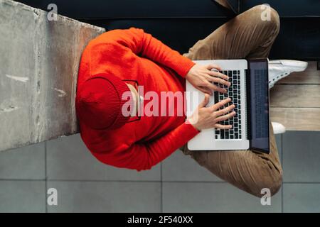 Freelancer man sitting on bench next by window legs crossed, online working on laptop. Distance job Stock Photo