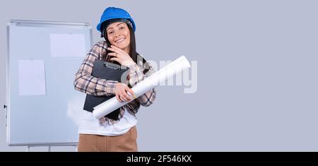 A business woman in a helmet with documents and a project in her hands solves business matters by phone. Banner and side blank space. Stock Photo