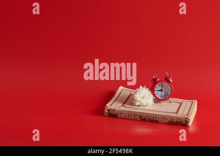 the alarm clock stands on a closed book on a red background Stock Photo