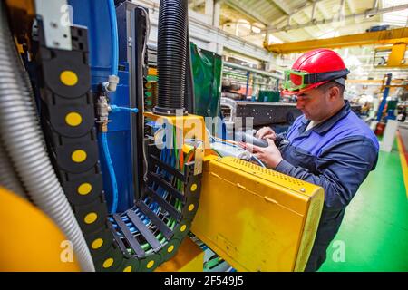 Ekibastuz, Kazakhstan: Rail car-building plant. Young Asian worker in red hardhat and plastic protective glasses programming CNC machine Stock Photo