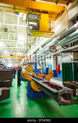 Ekibastuz, Pavlodar region, Kazakhstan: Railroad car-building plant workshop. Overhead crane with mechanical hand. crane operator woman in cabine. Stock Photo