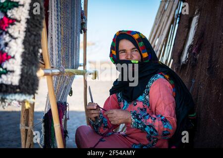 Erg Chebbi, Morocco - April 12, 2016: A berber woman weaves using a traditional loom in a village near the Erg Chebbi, in Morocco. Stock Photo