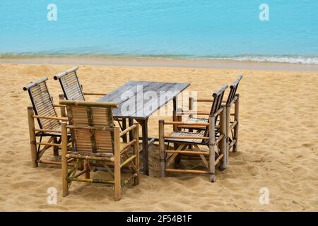 Wooden bamboo furniture, table and five chairs around on sand beach with blue sea water background in Koh Samui island, Thailand Stock Photo