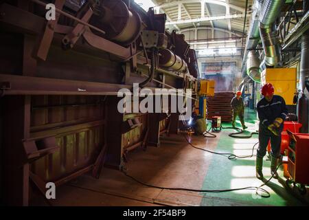 Ekibastuz, Pavlodar region, Kazakhstan: Rail car-building plant. Three welder workers in workshop.Yellow pipes air suction system