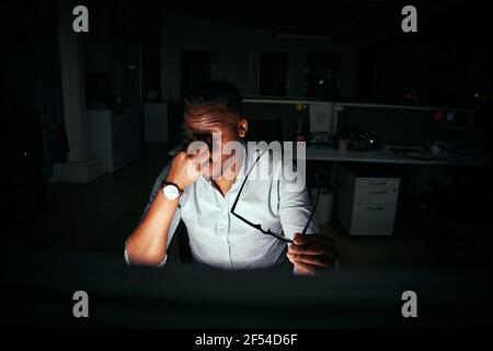 Frustrated young african businessman taking off eyeglasses and massaging his nose due to computer overwork in office Stock Photo