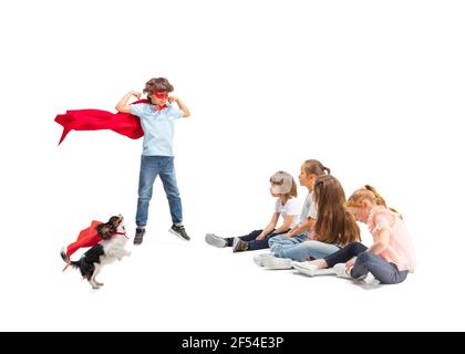 Power. Child pretending to be a superhero with his friends sitting around  him. Kids excited, inspired by their strong friend in red coat isolated on  white background. Dreams, emotions concept Stock Photo 