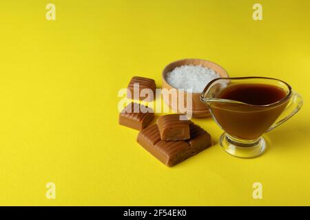 Caramel pieces, sauce and bowl of salt on yellow background Stock Photo