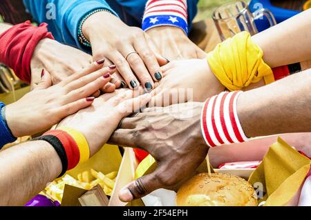Top side view of multiracial hands of football supporter friend sharing street food - Friendship concept with soccer fan enjoying food together Stock Photo