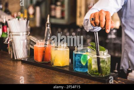Bartender hand at multicolored fashion drink with straw on vintage glass cups in fashion cocktail bar - Food and beverage concept Stock Photo