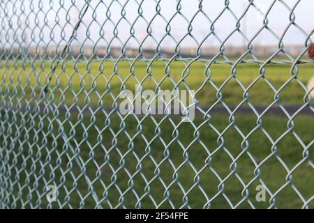 metallic mesh with green field behind, metal fence Stock Photo