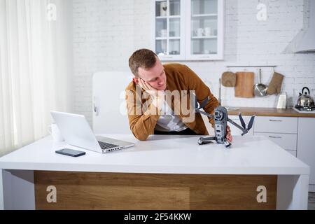 Handsome young businessman working with computer remotely sitting at the table in the kitchen. Nice happy man sitting in the room holding a drone in h Stock Photo