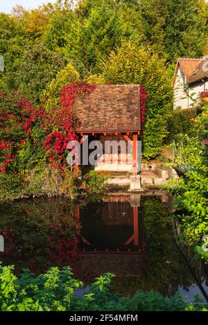 Old  lavoir (wash-house) over Fusain river in medieval town Chateau-Landon, France. Beautiful reflection of autumn ivy leaves in water. Stock Photo