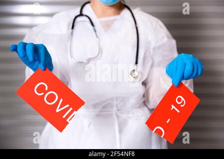 Close up of unrecognizable nurse with mask and protective gloves holding a broken card with the text Covid-19. Concept of the fight against Coronaviru Stock Photo