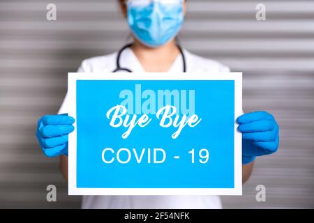 Close up of unrecognizable healthcare worker wearing a mask and protective gloves holding a sign with the text Bye Bye Covid-19. Concept of the end of Stock Photo