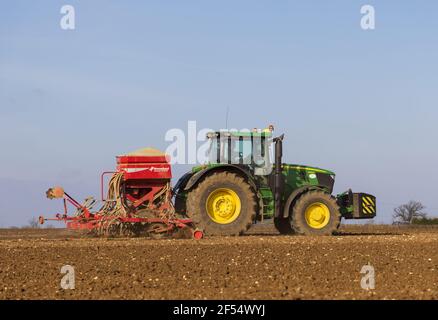 Farmer with a tractor in a field sowing seeds in early spring.  March 2021. Stock Photo