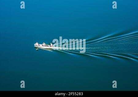 White fishing boat with three people on board floats in a lake. Stock Photo