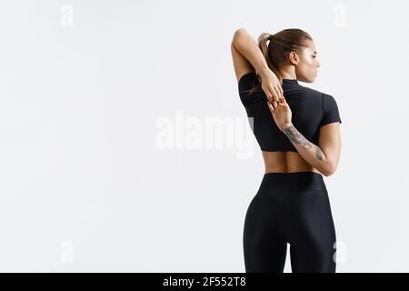 Rear view of healthy and fit sports woman stretching arms before exercising, looking away determined. Sportswoman doing warm up workout on white Stock Photo
