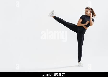 Confident female athlete workout, practice leg kicks, kicking air in sportswear. Muscular trained woman kicking with raised feet, exercise kickboxing Stock Photo