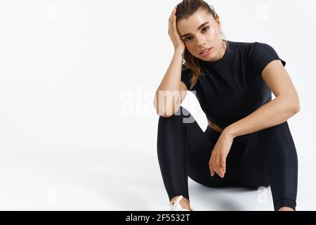 Sport and women. Female athlete sit on floor after workout. Fit healthy trained woman resting during fitness training session, look at camera, white Stock Photo