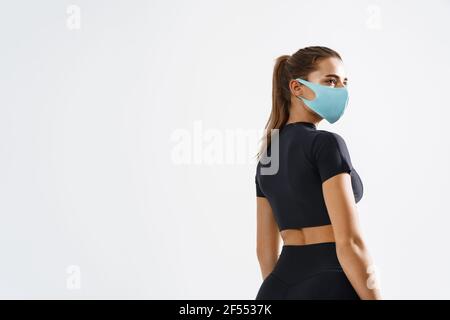 Rear view of confident fitness woman looking aside in protective face mask. Sporty female athlete with fit body, turn head and look away, workout Stock Photo