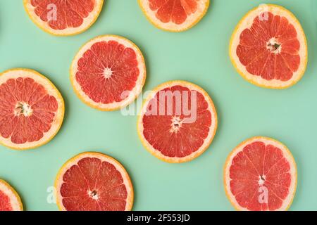 Grapefruit citrus pattern composition. Grapefruit slices with juice are scattered around on a green background with shadows. Summer or spring concept. Stock Photo
